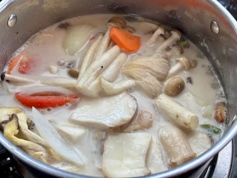 Vegetables and mushrooms cooked in a creamy tom kha hed broth inside a pot on the stove.