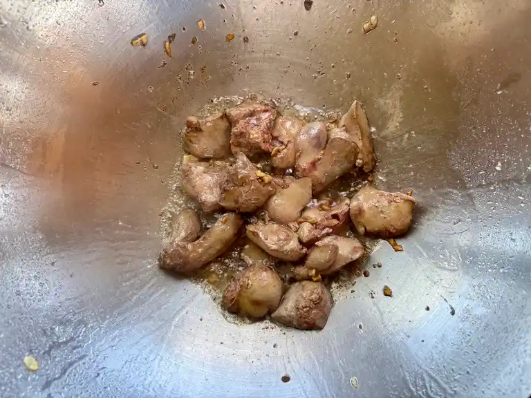 Partially cooked chicken liver in a stainless steel wok with sizzling garlic.