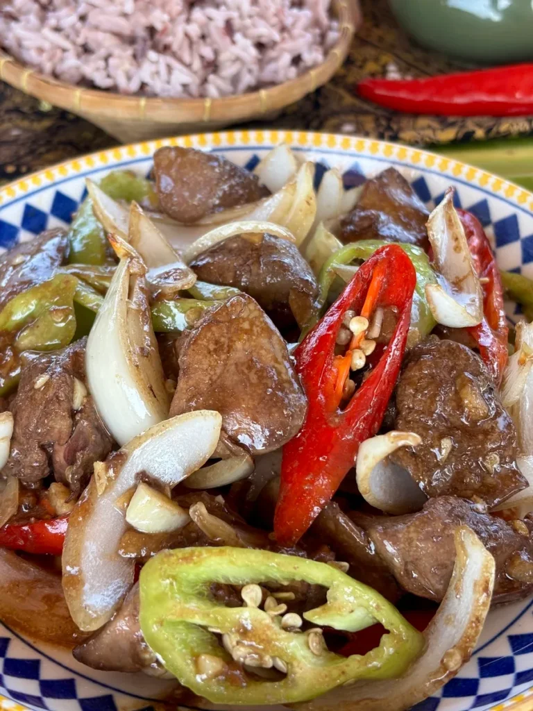 Close-up of pan-fried chicken liver with vibrant red and green chillies and caramelized onions.