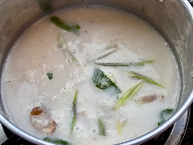 Boil the tom kha hed broth in a pot with lemongrass, galangal and kaffir lime leaves floating on the surface.