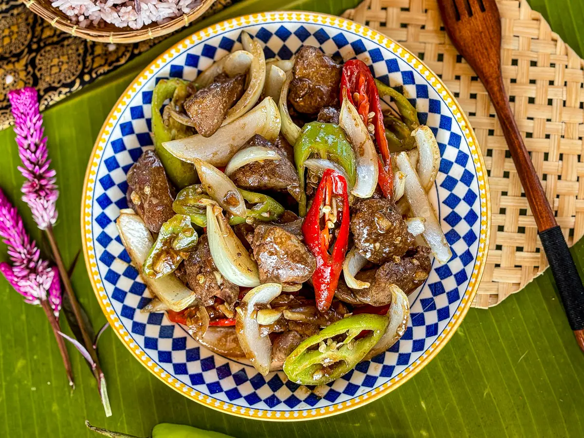 Overhead shot of chicken liver stir fry garnished with chilies, served with rice on a banana leaf placemat.