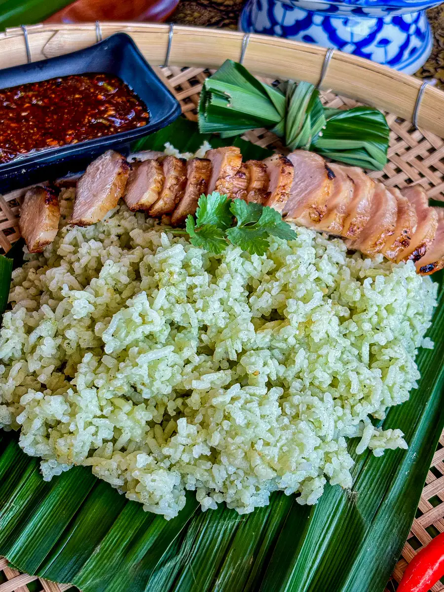 A serving of aromatic pandan rice on a bamboo tray, garnished with coriander and served with grilled meat.