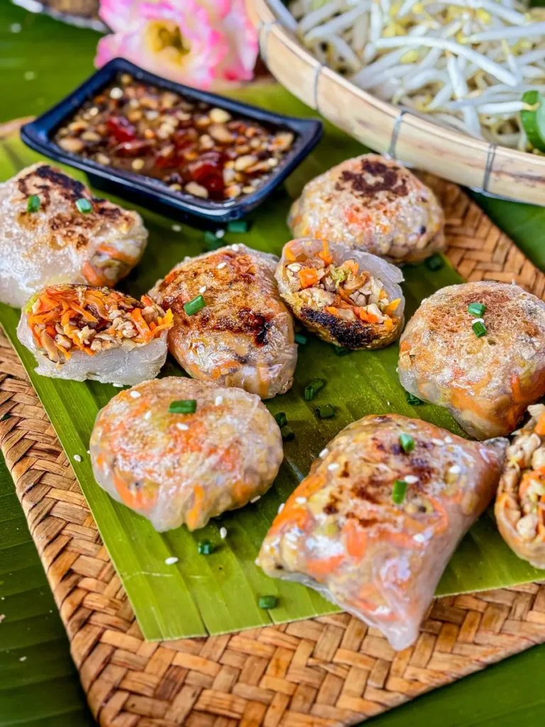 Golden-brown pan-fried rice paper dumplings filled with a meat and vegetable mixture, garnished with sesame seeds and spring onions.