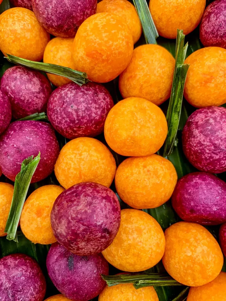 Thai sweet potato balls (kanom kai nok krata) made with orange and purple sweet potatoes, served with pandan leaves.