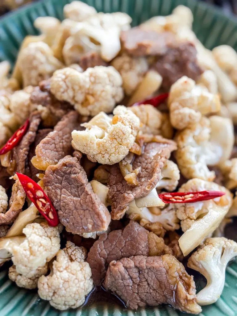 Close-up of beef cauliflower stir-fry with sauce and red chilies.