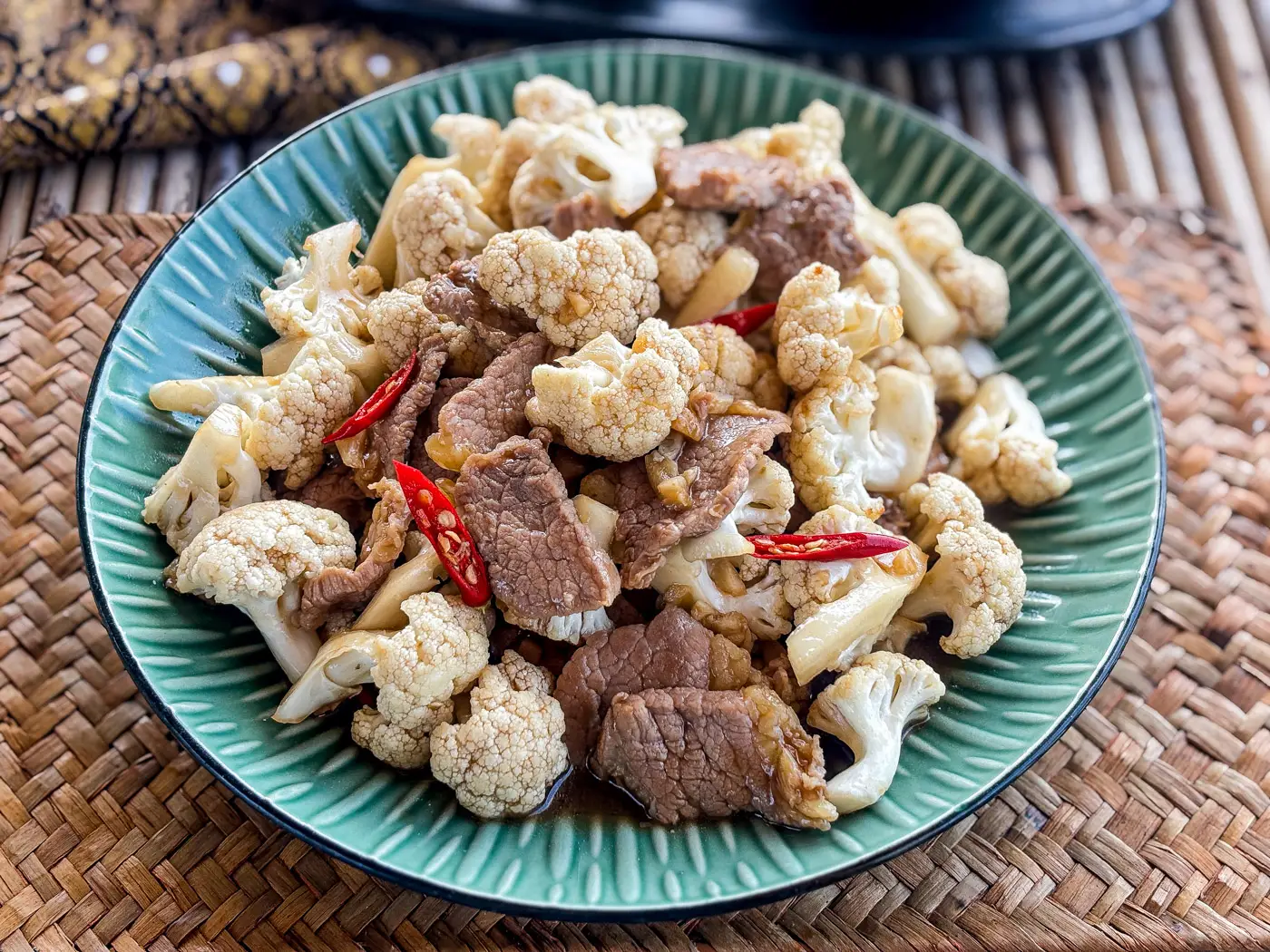 Cauliflower beef stir-fry with red chili slices served on a green dish.