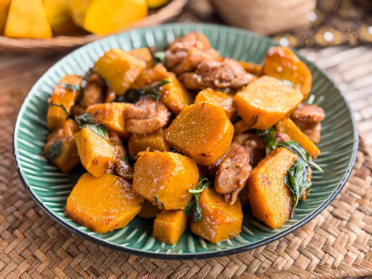 Thai chicken and pumpkin stir-fry served on a green plate, topped with basil leaves.