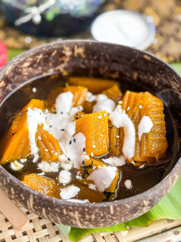 Fak thong cheum served in a rustic coconut bowl, drizzled with creamy coconut milk and sprinkled with sesame seeds