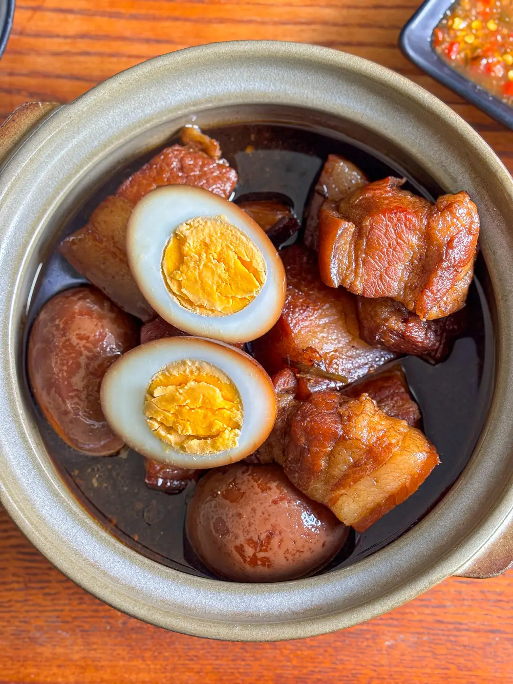 Thai moo palo with braised pork belly and soy-stewed eggs in a clay pot, showing glossy skin and rich, dark broth.