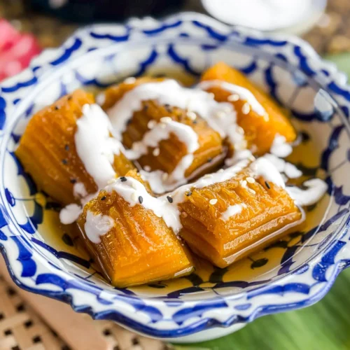 Thai pumpkin in syrup (fak thong cheum) in a patterned blue and white bowl, topped with coconut cream and sesame seeds.