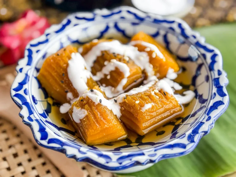 Thai pumpkin in syrup (fak thong cheum) in a patterned blue and white bowl, topped with coconut cream and sesame seeds.