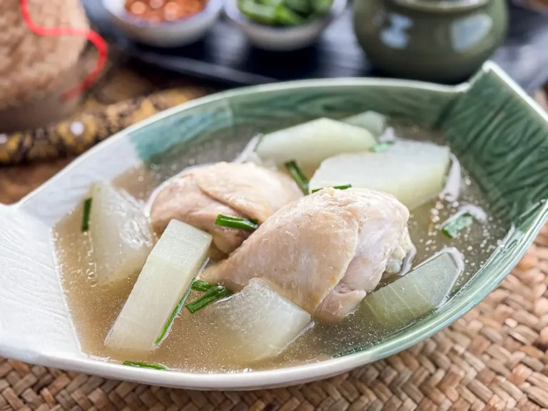 Thai winter melon soup with chicken served in a deep green bowl, garnished with green onion.