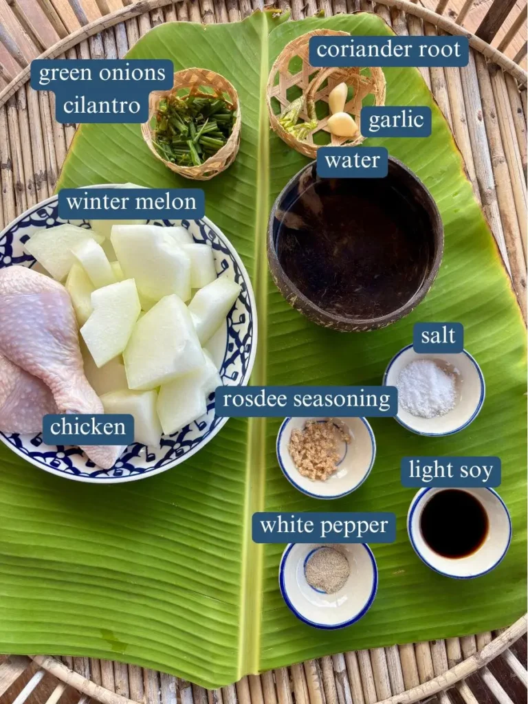 Seen above the head of the ingredients for the winter melon soup, including winter melon, chicken berries, coriander root, garlic, water, salt, rosdee dressing, light soy sauce, white pepper, coriander and green onions on banana leaves.