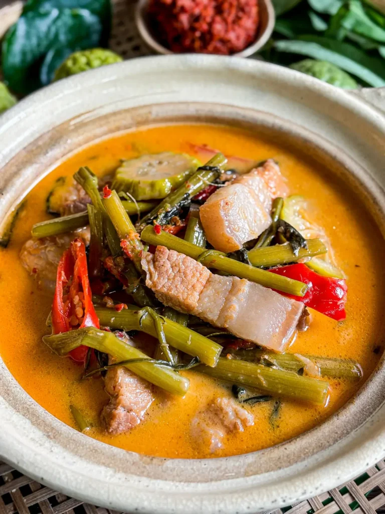 Thai red curry pork belly (gaeng tepo) with tender pork belly, morning glory, and red curry broth in a clay pot.