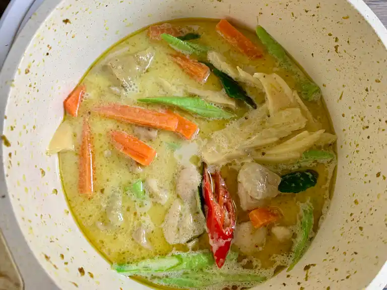 Carrots, yard long beans, bamboo shoots, and chili simmering in Thai green curry broth.