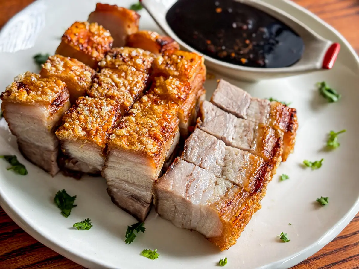 Crispy pork belly pieces cooked in the air fryer, plated with a soy-based dipping sauce.
