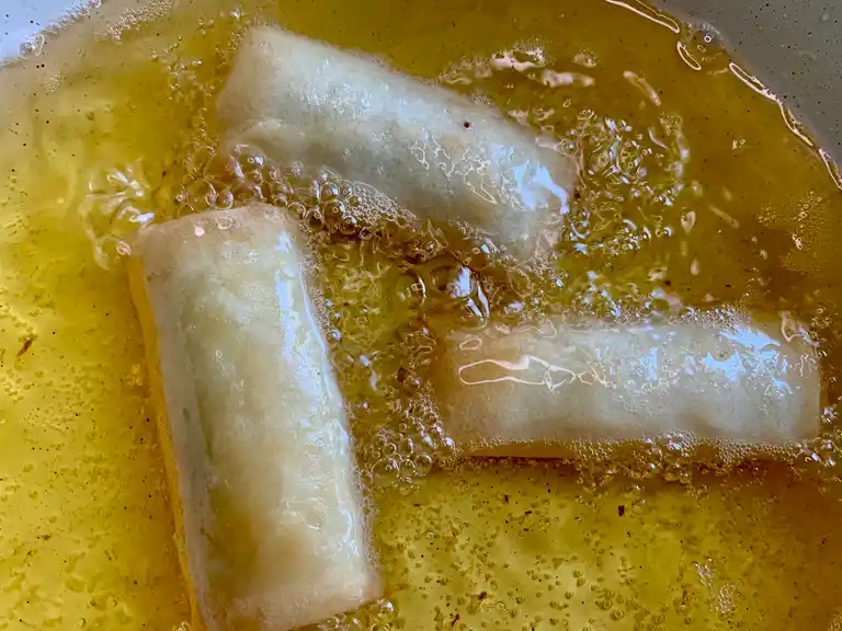 Banana spring rolls being deep-fried in hot oil until golden brown.