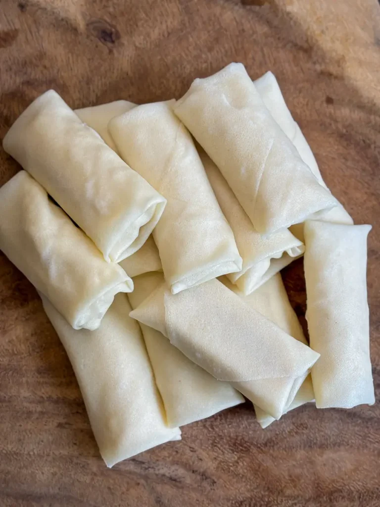 Uncooked banana spring rolls neatly wrapped and stacked on a wooden surface.