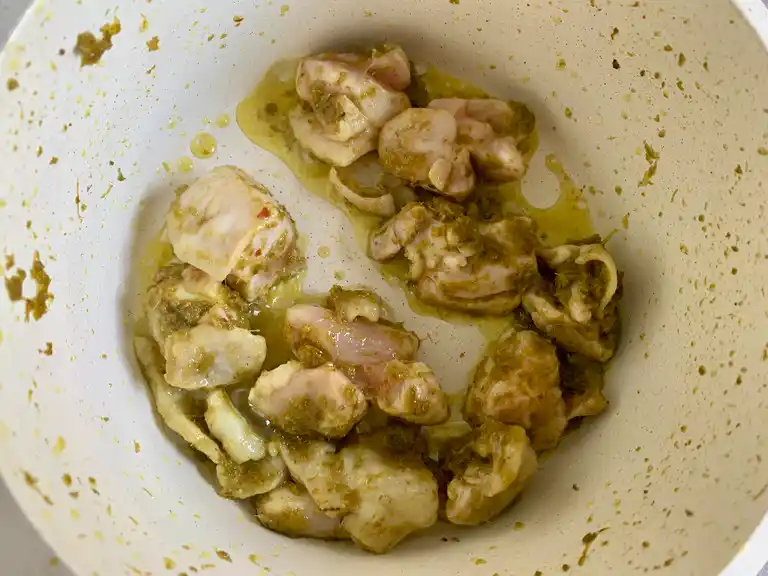 Bite-sized chicken pieces cooking in green curry paste inside a pot.