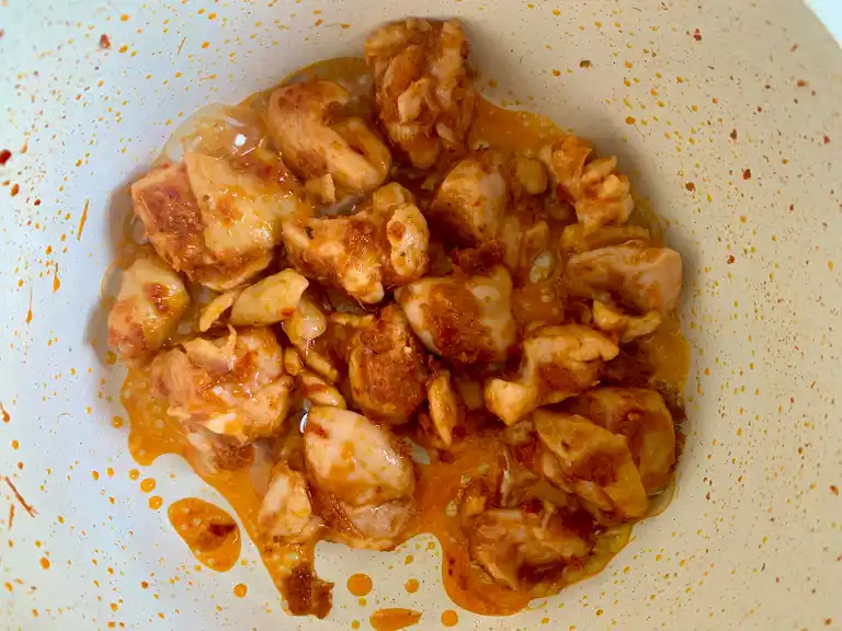 Pedaços de frango cozinhando em pasta de curry vermelho até revestir.