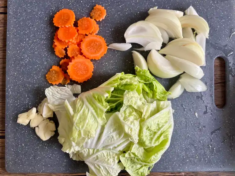 Chopped napa cabbage, carrots, onion, and garlic on a cutting board.