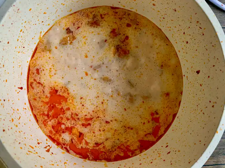 O leite de coco ferve com frango e pasta de curry em uma panela.