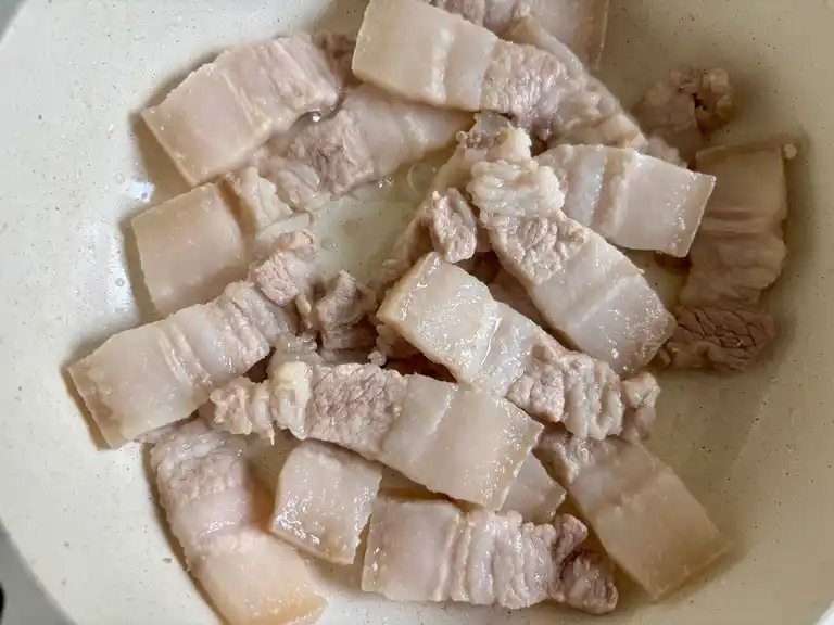 Pork belly pieces cooking in a pan of water.