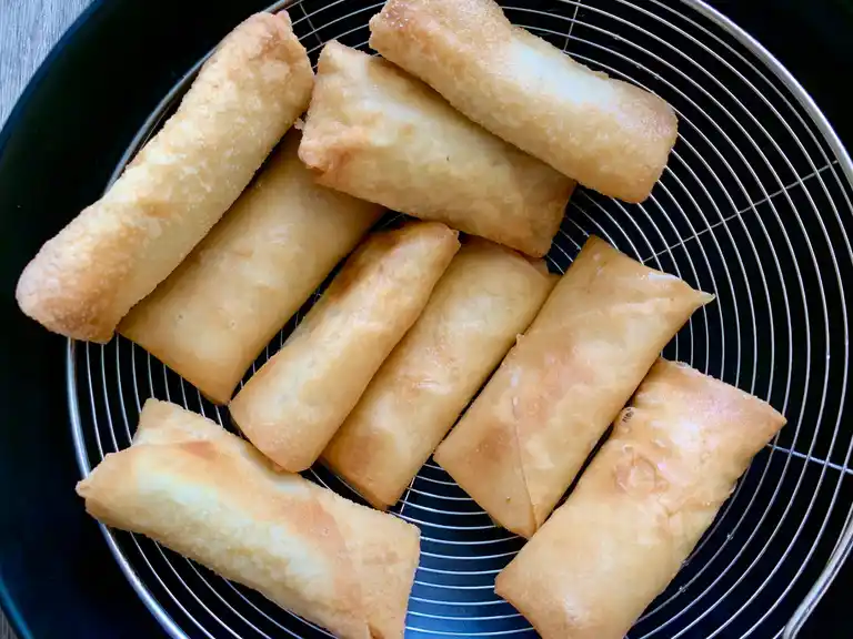 Freshly fried banana spring rolls resting on a wire rack to drain excess oil.