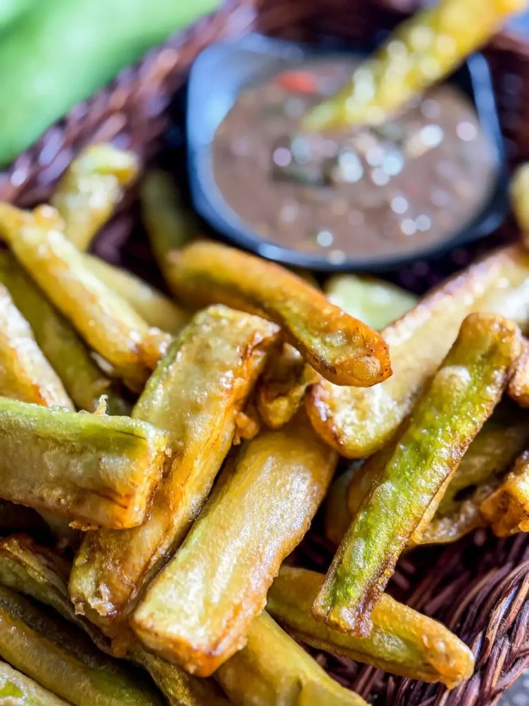 Close-up of golden fried eggplant fries served in a basket with Thai nam prik kapi dipping sauce in the background.