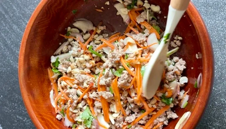 Mixing ground pork with carrots, shallots, peanuts, and herbs in a wooden bowl.