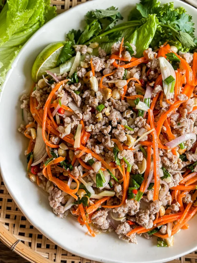 Close-up of nam sod Thai ginger pork salad with ground pork, peanuts, carrots, and herbs on a white plate.