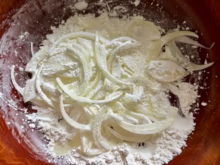 Raw onion slices tossed in cornstarch in a large mixing bowl.