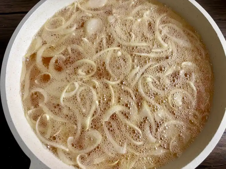 Onion slices frying in hot oil inside a large pan.