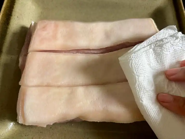 Hand patting pork belly skin dry with a paper towel.