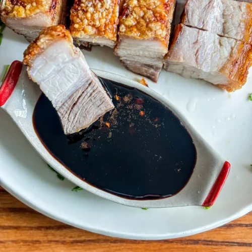 Crispy air fryer pork belly served with a dark soy dipping sauce on a white plate.