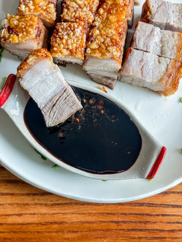 Crispy air fryer pork belly served with a dark soy dipping sauce on a white plate.