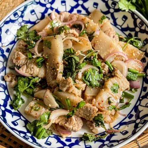 Thai pork belly larb in a traditional patterned bowl, mixed with fresh cilantro, mint, green onions, and sliced shallots.