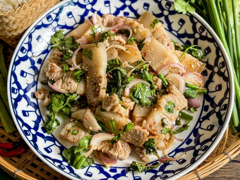 Thai pork belly larb in a traditional patterned bowl, mixed with fresh cilantro, mint, green onions, and sliced shallots.