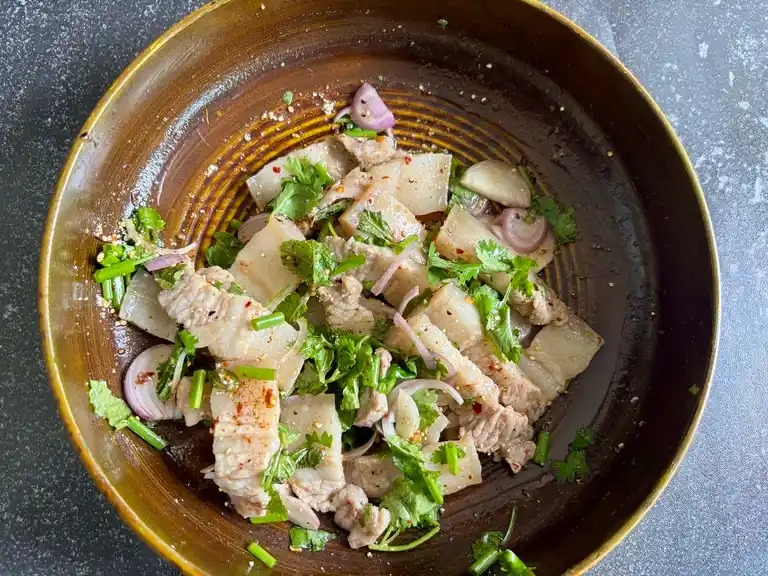 Cooked pork belly mixed with herbs and shallots in a bowl.