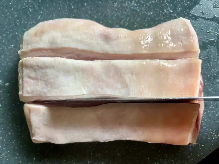 Pork belly with deep cuts across the skin before cooking.