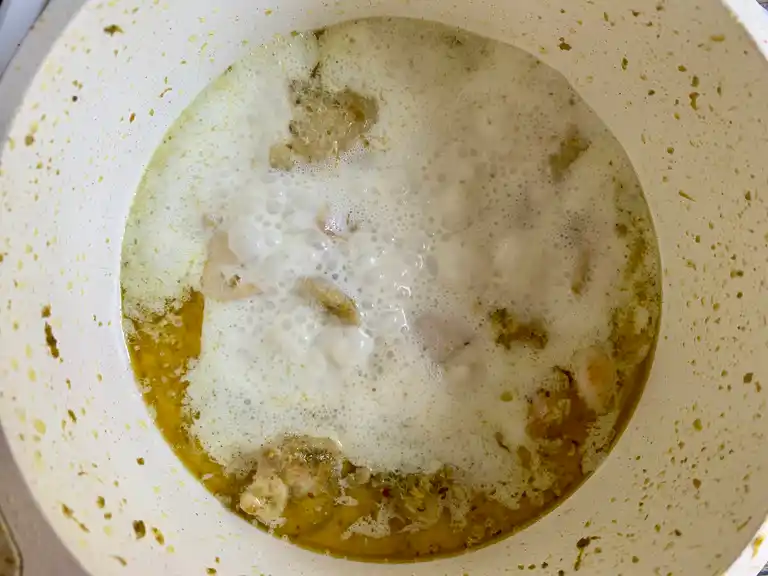 Chicken simmering in coconut milk and green curry paste in a bubbling pot.