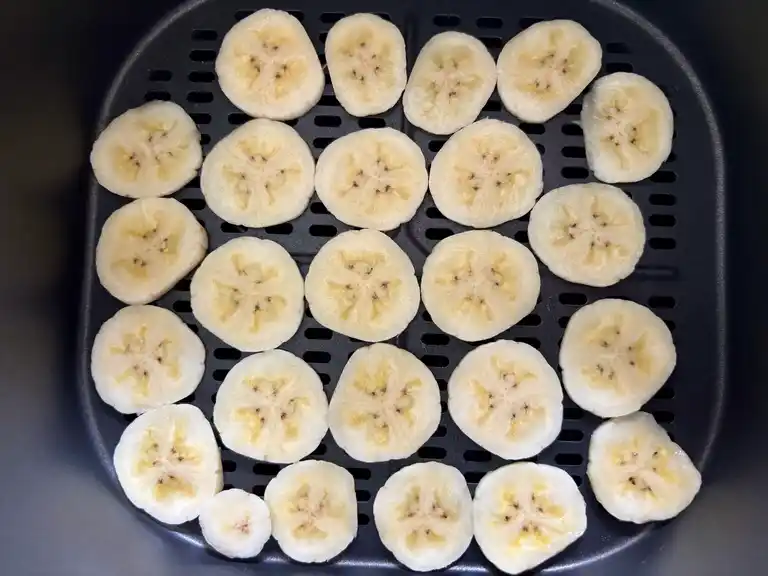 Sliced bananas neatly arranged in a single layer in the air fryer basket before cooking.