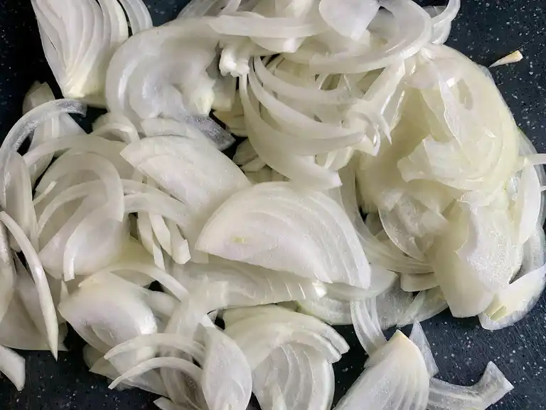 Thinly sliced white onions on a black cutting board.