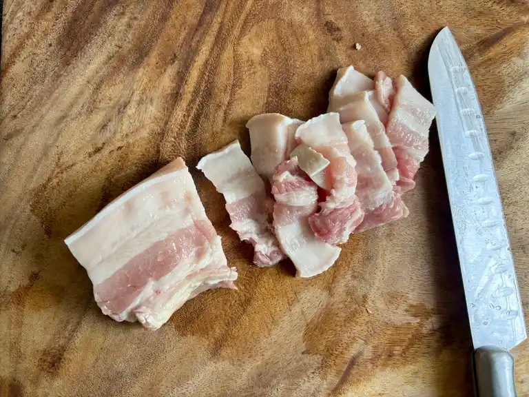 Raw pork belly slices on a cutting board with a knife..