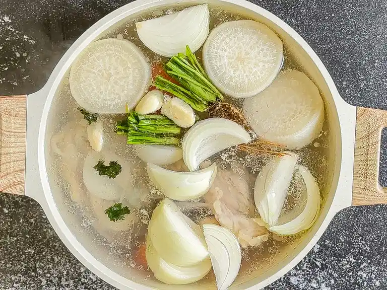Pot of water with daikon, onion, garlic, and coriander root simmering.