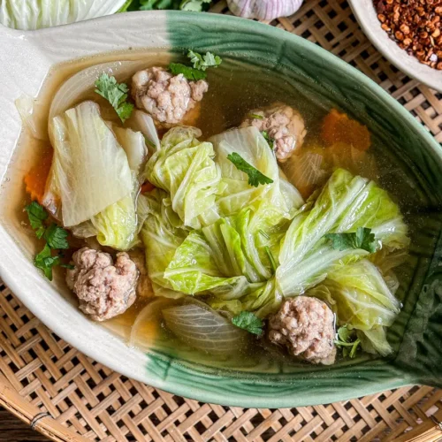 Thai cabbage soup with napa cabbage, pork meatballs, and clear broth, garnished with fresh herbs.