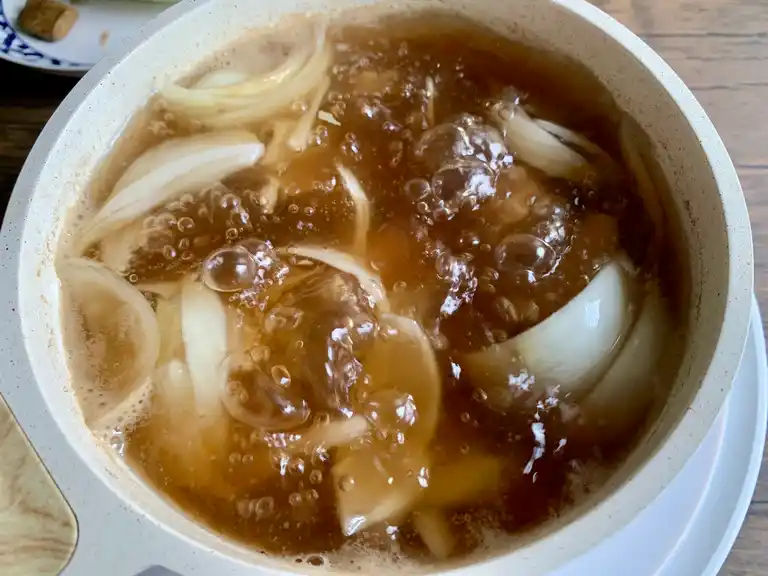 Pot of Thai cabbage soup broth simmering with sliced onions.