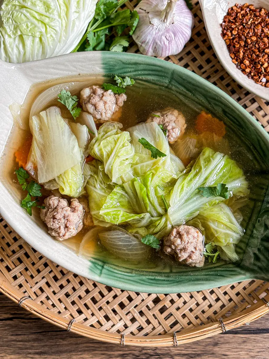 Thai cabbage soup with napa cabbage, pork meatballs, and clear broth, garnished with fresh herbs.