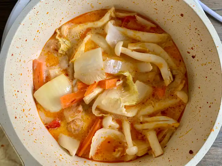 Repolho, cenoura, cogumelos e chili fervendo em caldo de curry vermelho.