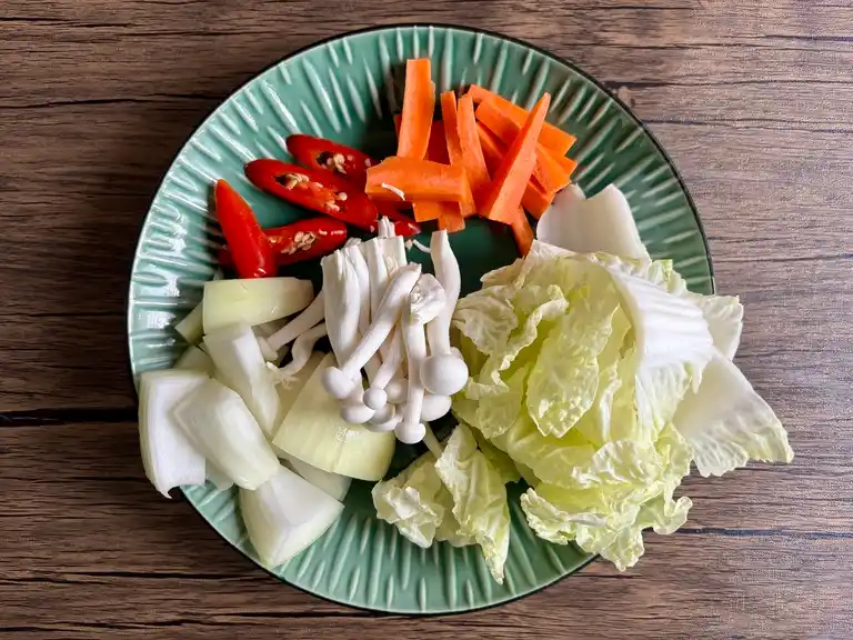 Vegetais frescos, incluindo repolho, cenoura, cebola, cogumelos e pimenta preparados em um prato.